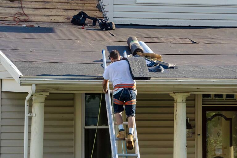 Workers install roofing while attic insulation and ventilation improvements are visible beneath the roof deck.